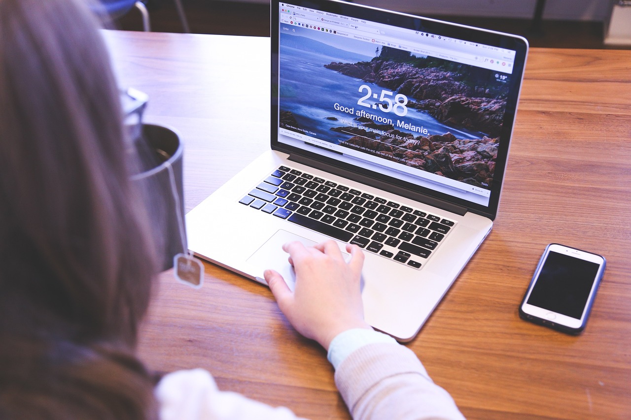 Eine Person tippt auf einem Macbook. Auf dem Display ist eine Startoberfläche zu sehen, die "Good afternoon, Melanie" wünscht.